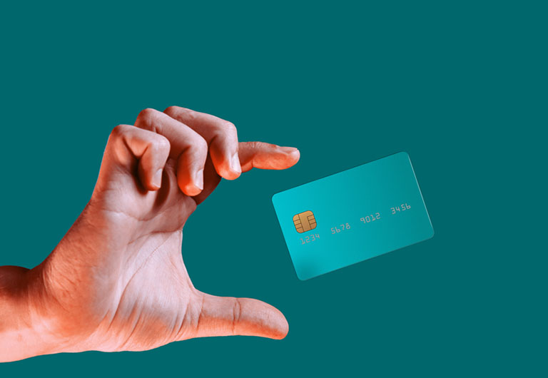 A credit card floating in the air between the thumb and the index finger of a hand against a teal background