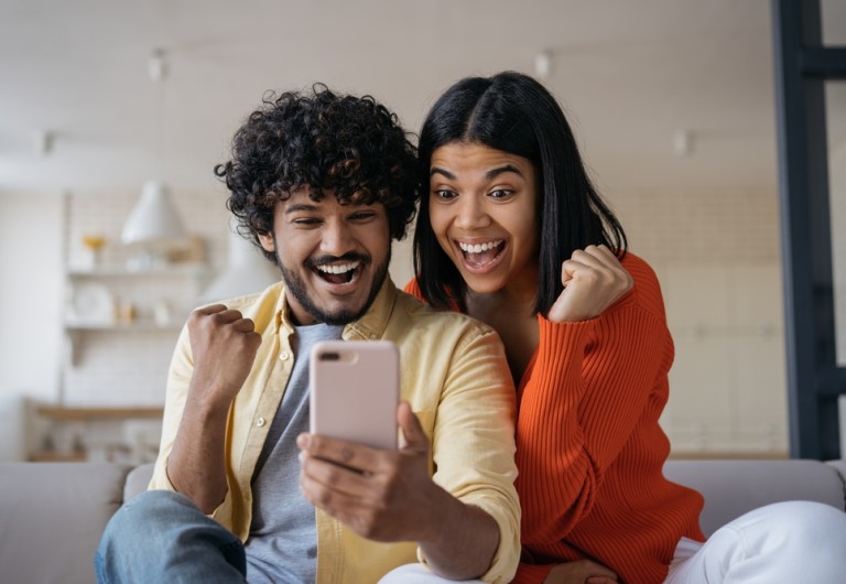 Man and woman cheering looking at their mobile phone