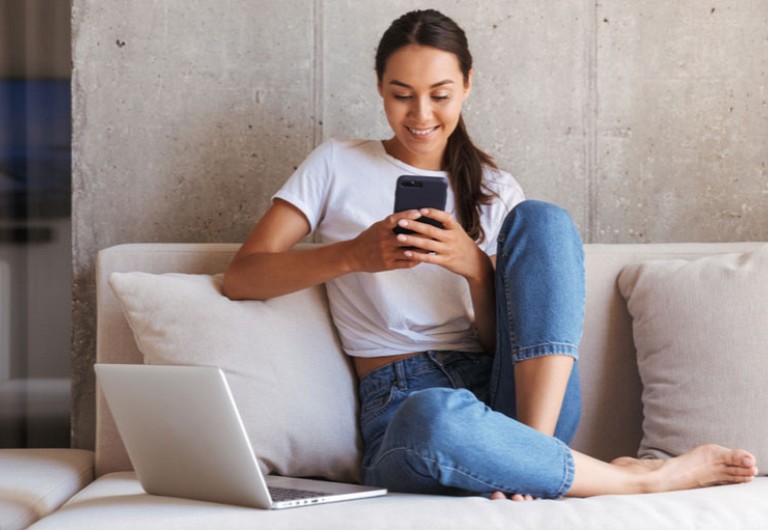 Woman sitting in a sofa looking at her mobile phone and smiling