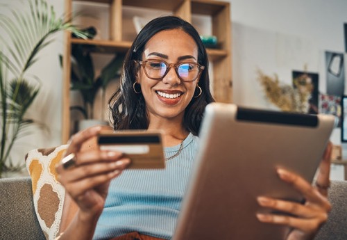 Smiling woman holding a tablet in one hand and a credit card in the other
