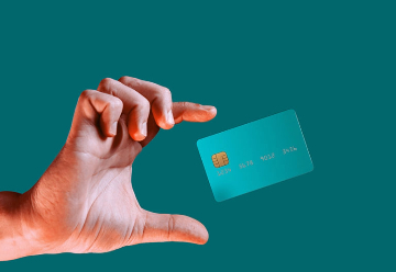 Une carte de crédit flottant dans l'air entre le pouce et l'index d'une main sur un fond bleu sarcelle