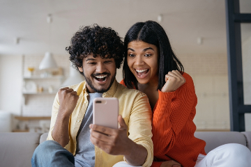 Mann und Frau schauen jubelnd auf ihr Mobiltelefon