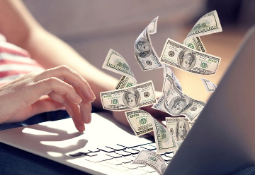 A laptop with a person typing on it while dollar bills fly out of the laptop screen