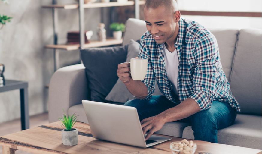 Man holding a cup of coffee while checking his laptop