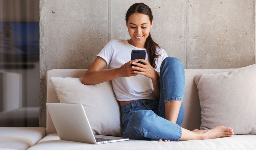 Woman sitting in a sofa looking at her mobile phone and smiling