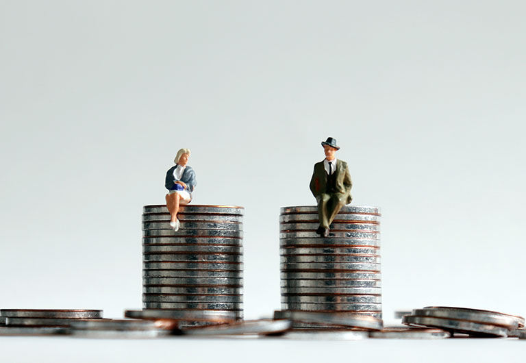 A miniature man and a miniature woman sitting on a stack of coins of the same height