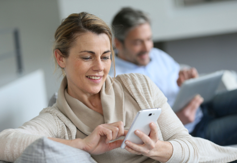 woman and man sitted on sofa check their phones while smiling