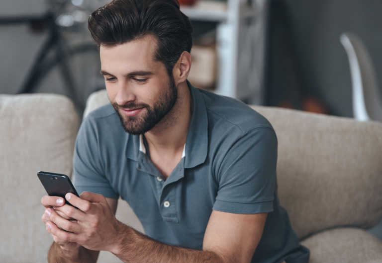 man sitted on a sofa checking his cell phone