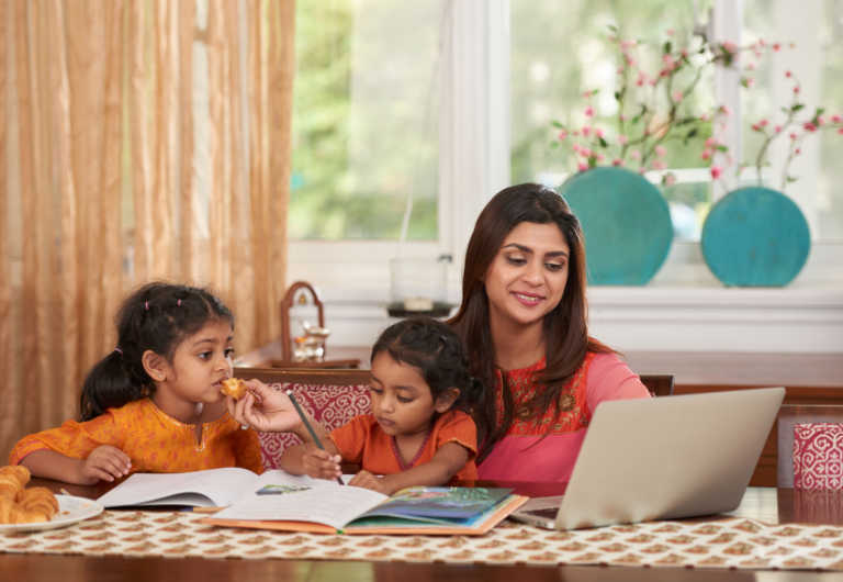 indian woman having lunch with her two children while checking her laptop
