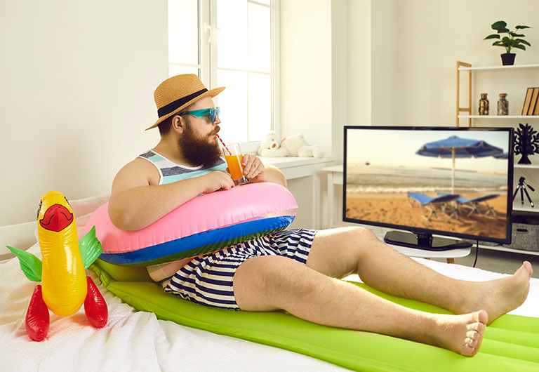 man sitted on a towel pretting his living room is the beach