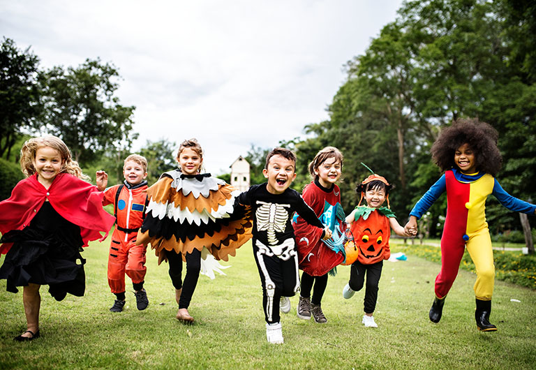 group of children dressed in Halloween costumes running through a green field