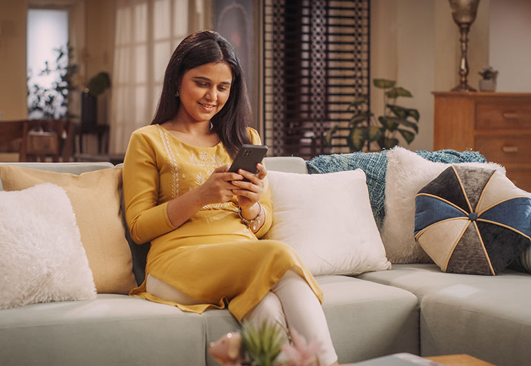 Smiling woman sitting on a sofa with a mobile phone in her hand