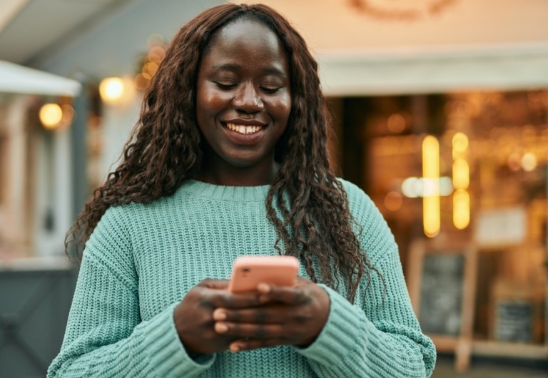 Woman standing outside smiling and looking at her mobile phone