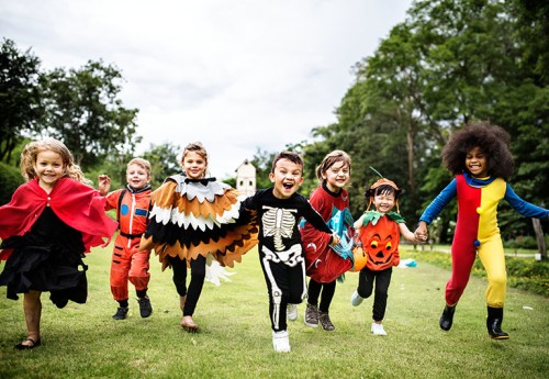 group of children dressed in Halloween costumes running through a green field